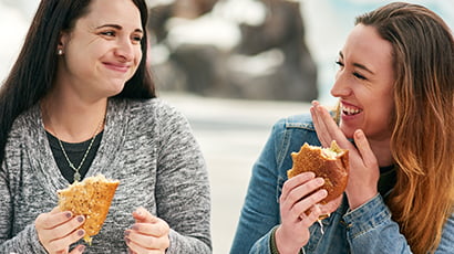 Two women are eating a sandwich in front of a building.