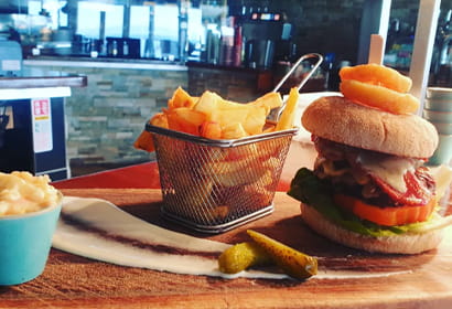 A burger with fries and chips on a wooden cutting board.