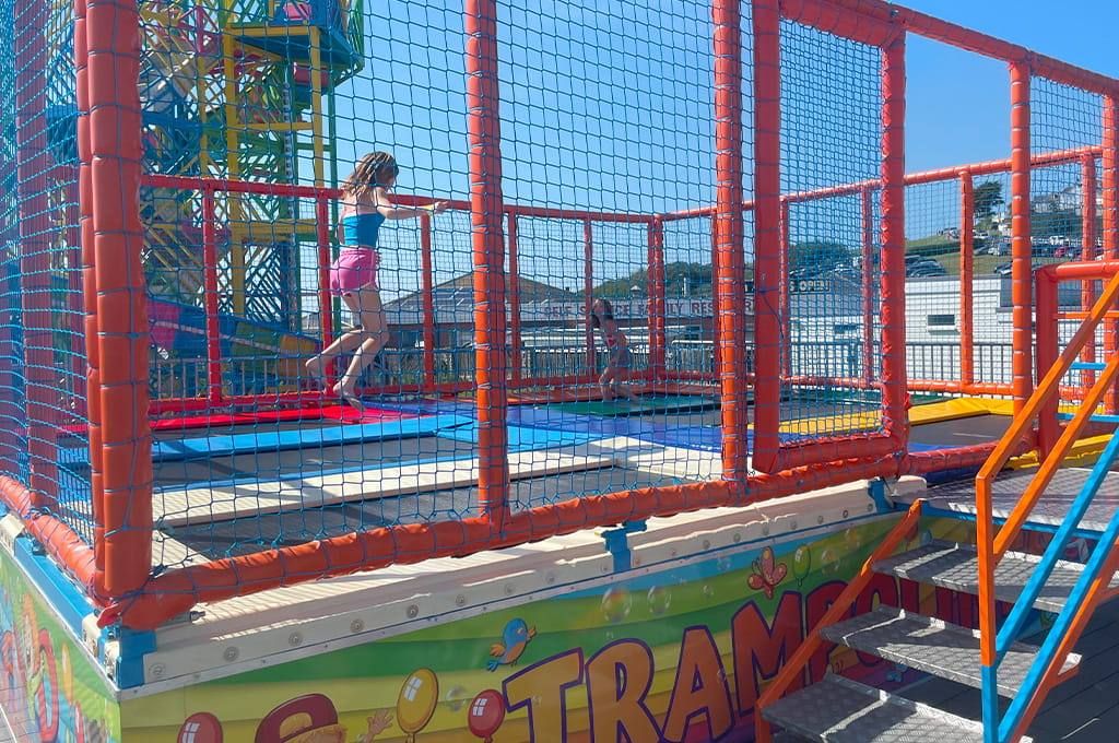 A girl is jumping on a trampoline at an amusement park.