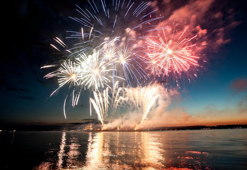 Fireworks exploding over a body of water.